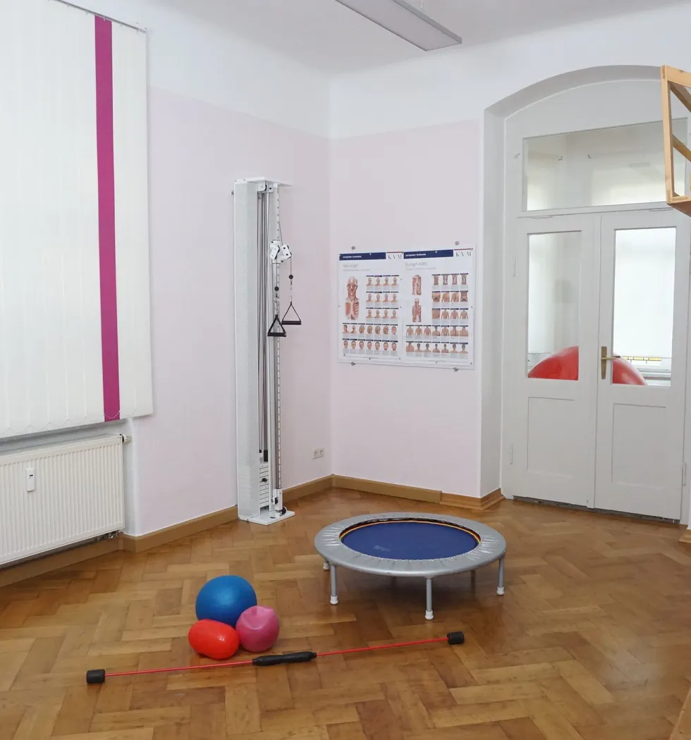 Sportraum für Bewegungstherapie mitTrampolin, Flexibars und Bällen. Im Hintergrund ein Zugerät und anatomische Schaubilder.
